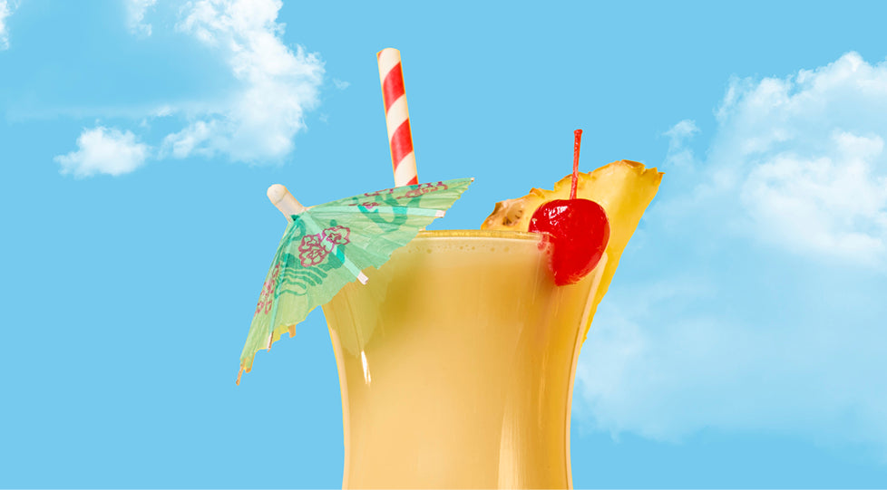 Tropical cocktail with a straw, umbrella, and cherry against a blue sky.